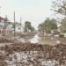 Calle inundada con agua fangosa y escombros tras lluvias torrenciales en zona urbana.