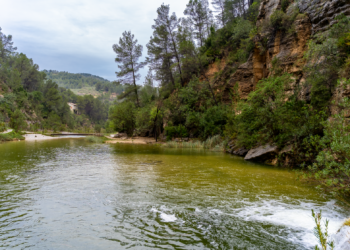 Río de montaña desbordado arrastrando escombros tras lluvias torrenciales en zona montañosa.