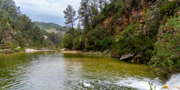 Río de montaña desbordado arrastrando escombros tras lluvias torrenciales en zona montañosa.